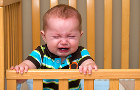 Baby crying in crib. Itchy eczema can cause sleep loss.