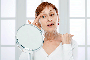 Mature woman with finger on eyelid looking into a mirror.